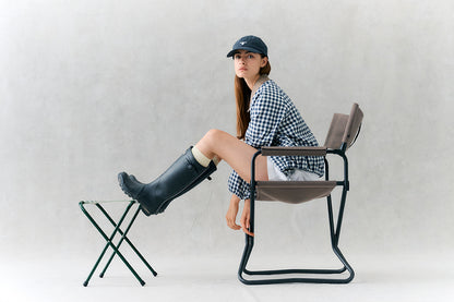 Person sitting on a modern chair with one leg on a small stool against a plain background