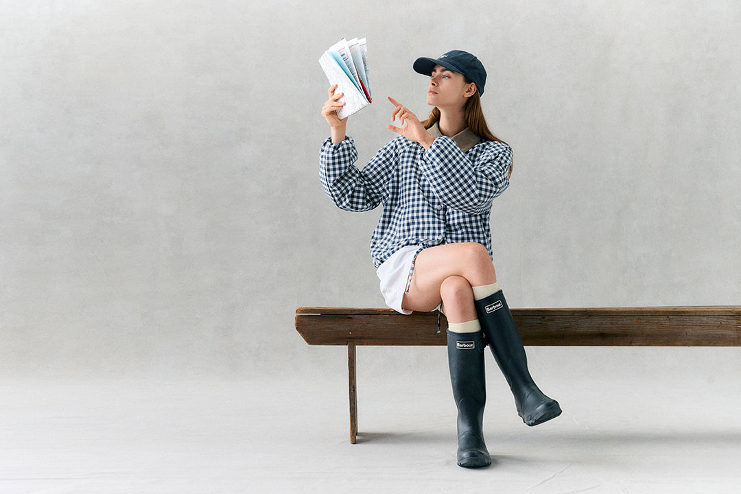 Person sitting on a bench wearing checkered shirt, white shorts, and black rain boots, holding color swatches.