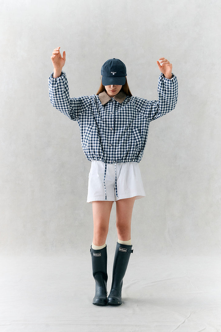 Person wearing a checkered shirt, white shorts, and black rain boots against a plain background