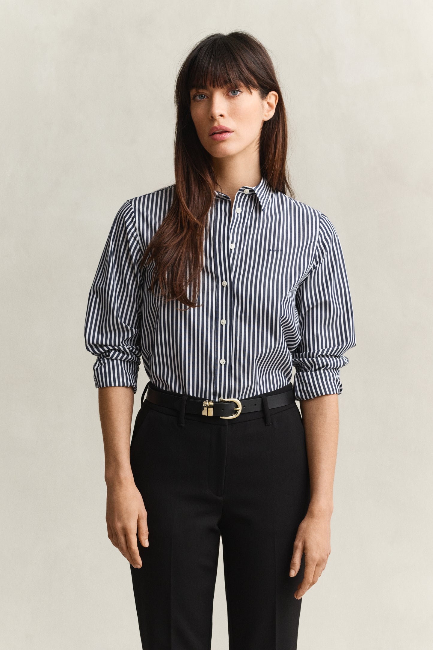 Woman wearing a striped shirt and black pants against a plain background