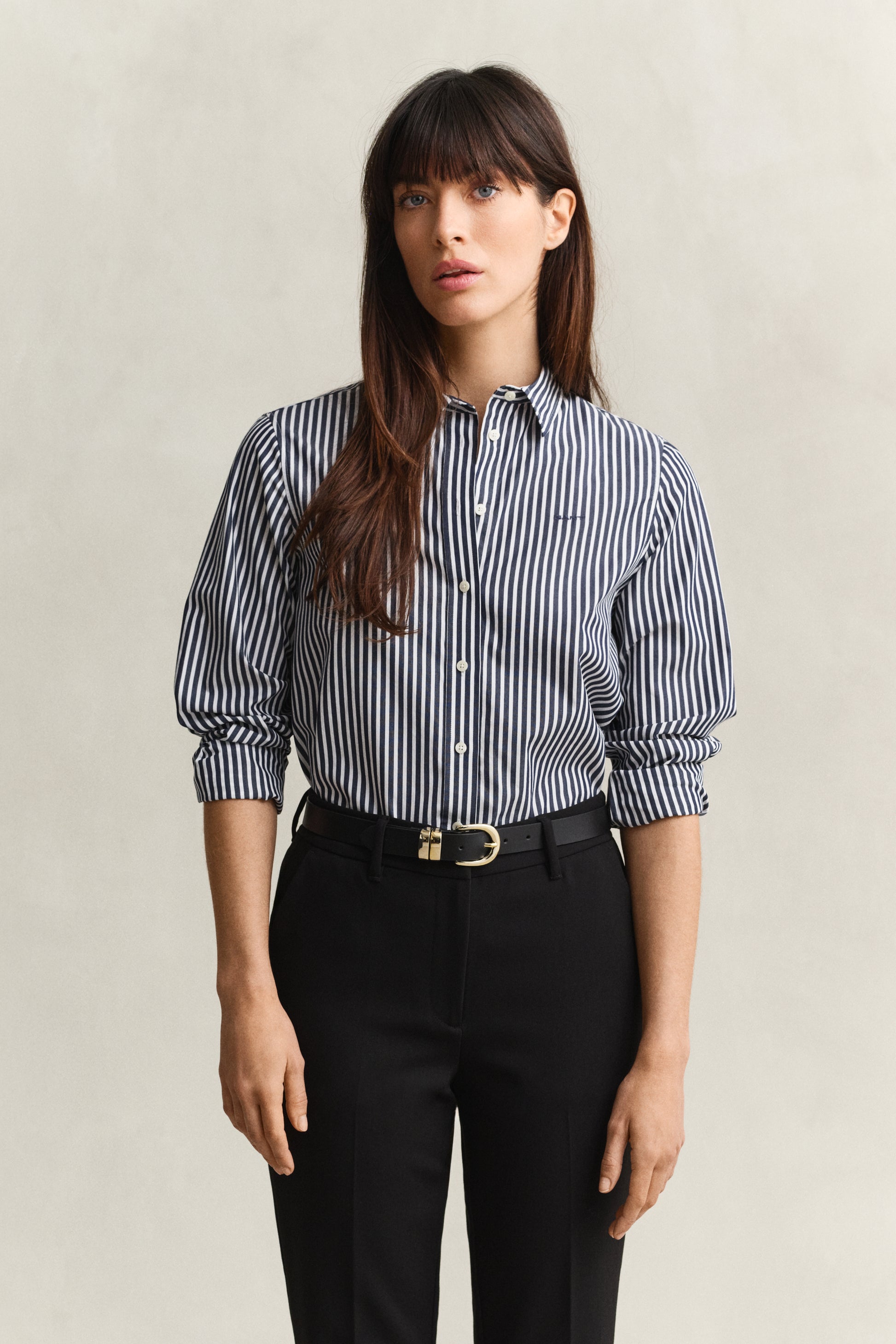 Woman wearing a striped shirt and black pants against a plain background
