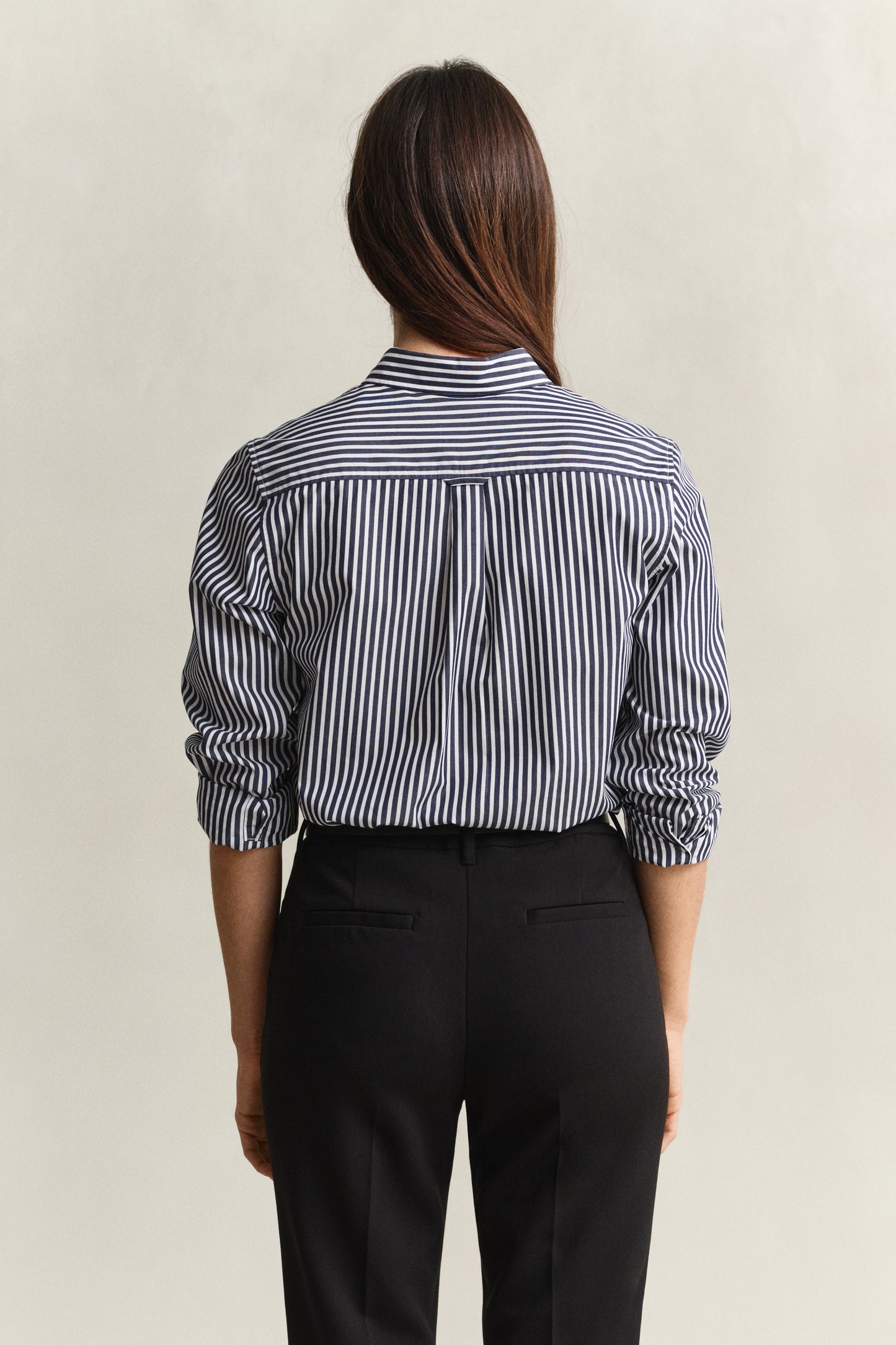 Person wearing a black and white striped shirt with rolled-up sleeves and black pants on a beige background