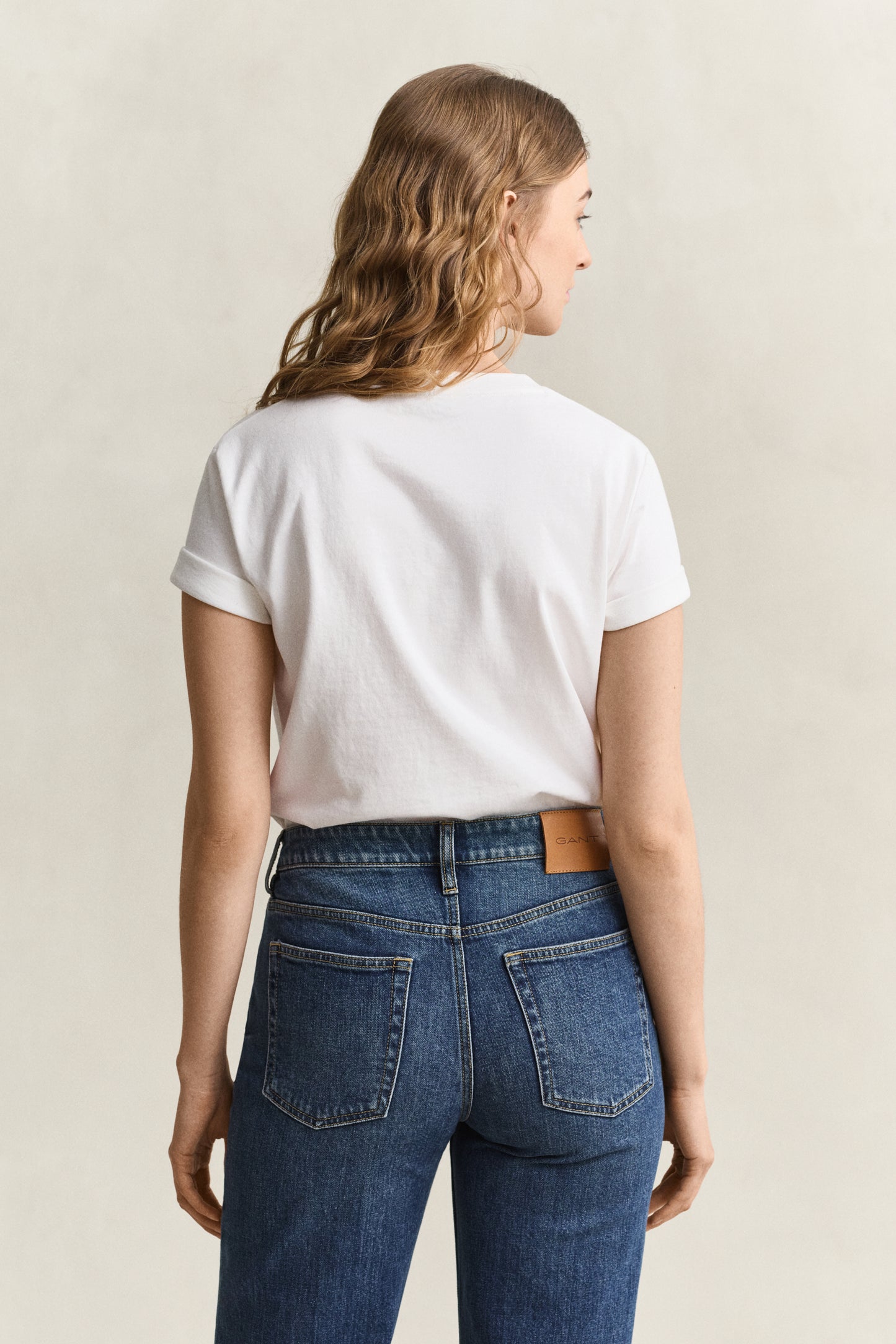 Person wearing a white t-shirt and blue jeans on a beige background