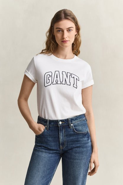Woman wearing a white Gant t-shirt and blue jeans against a beige background