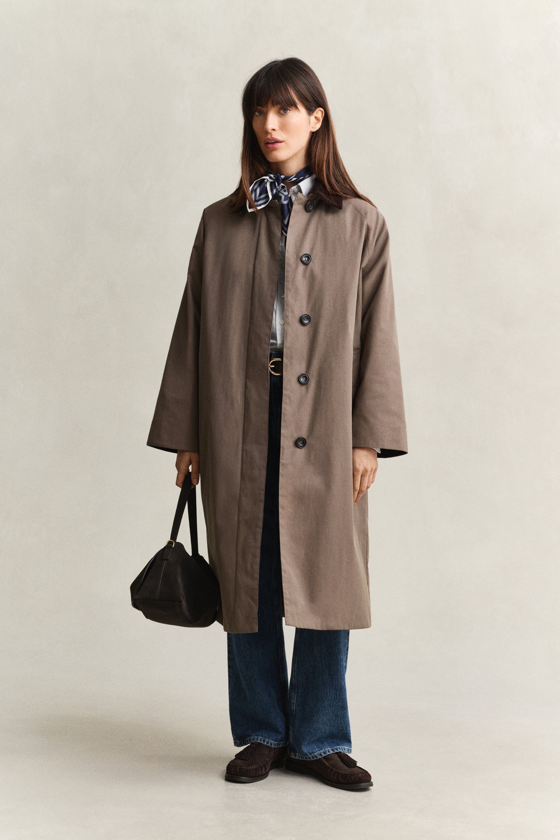 Woman wearing a brown coat holding a black bag on a plain background