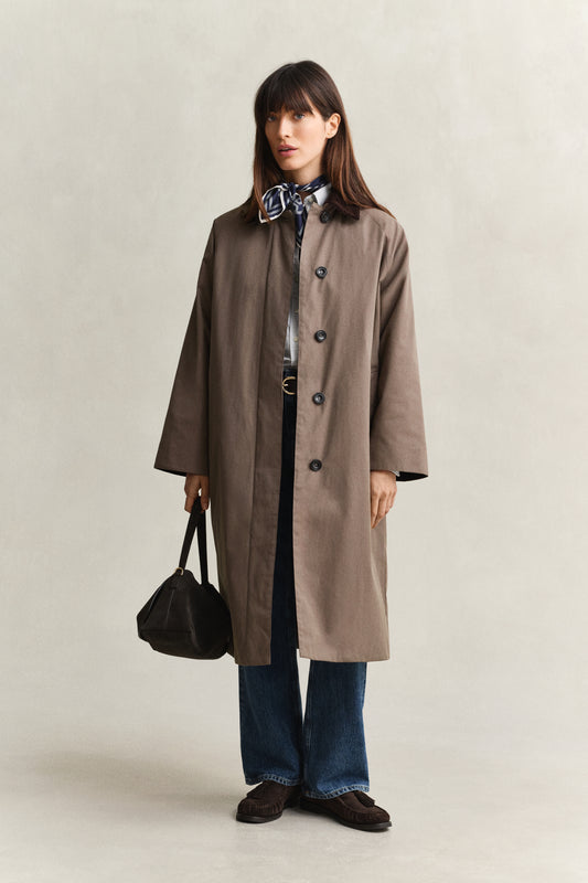 Woman wearing a brown coat holding a black bag on a plain background