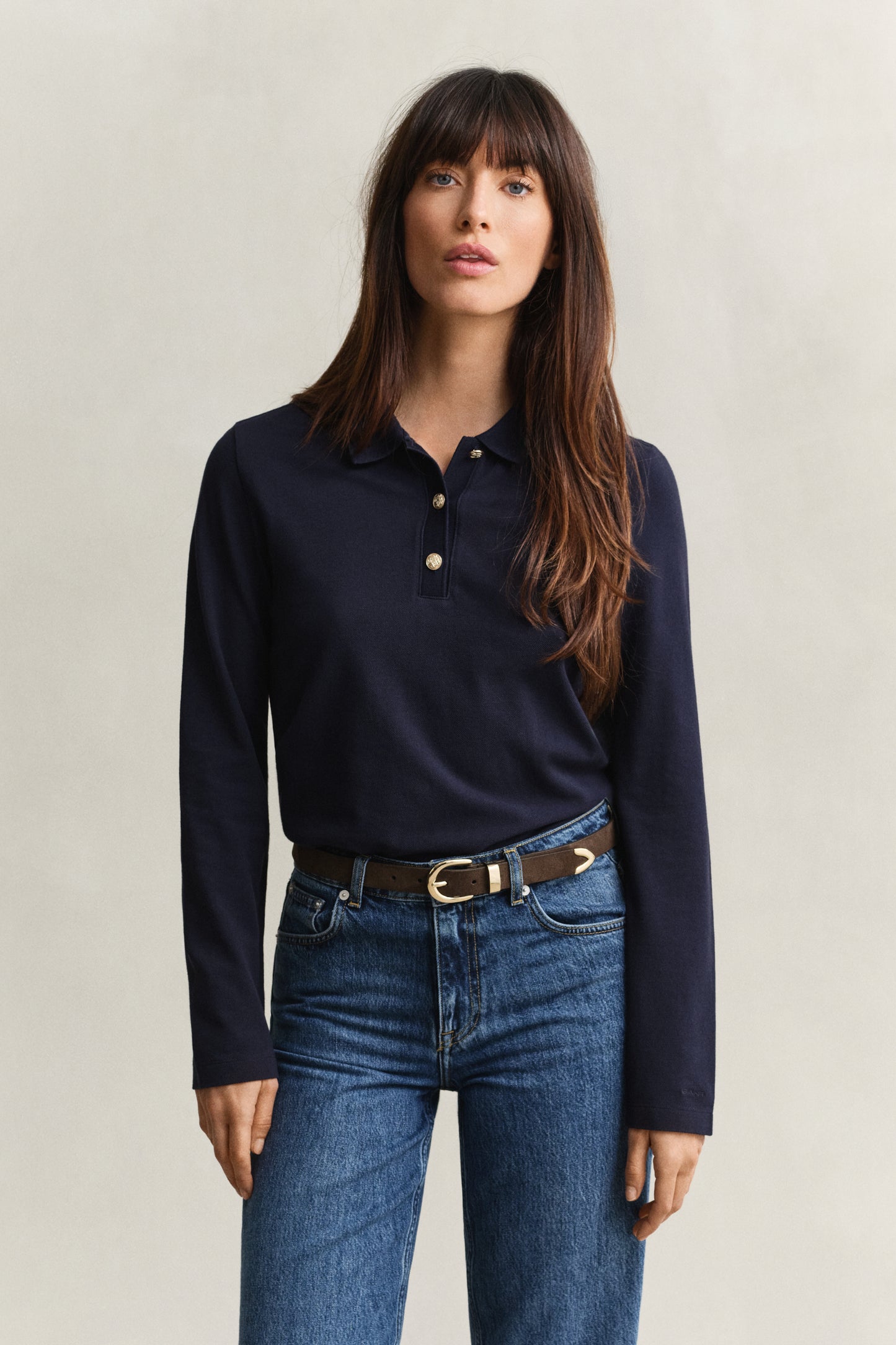 Woman wearing a navy long-sleeve polo shirt and blue jeans against a plain background