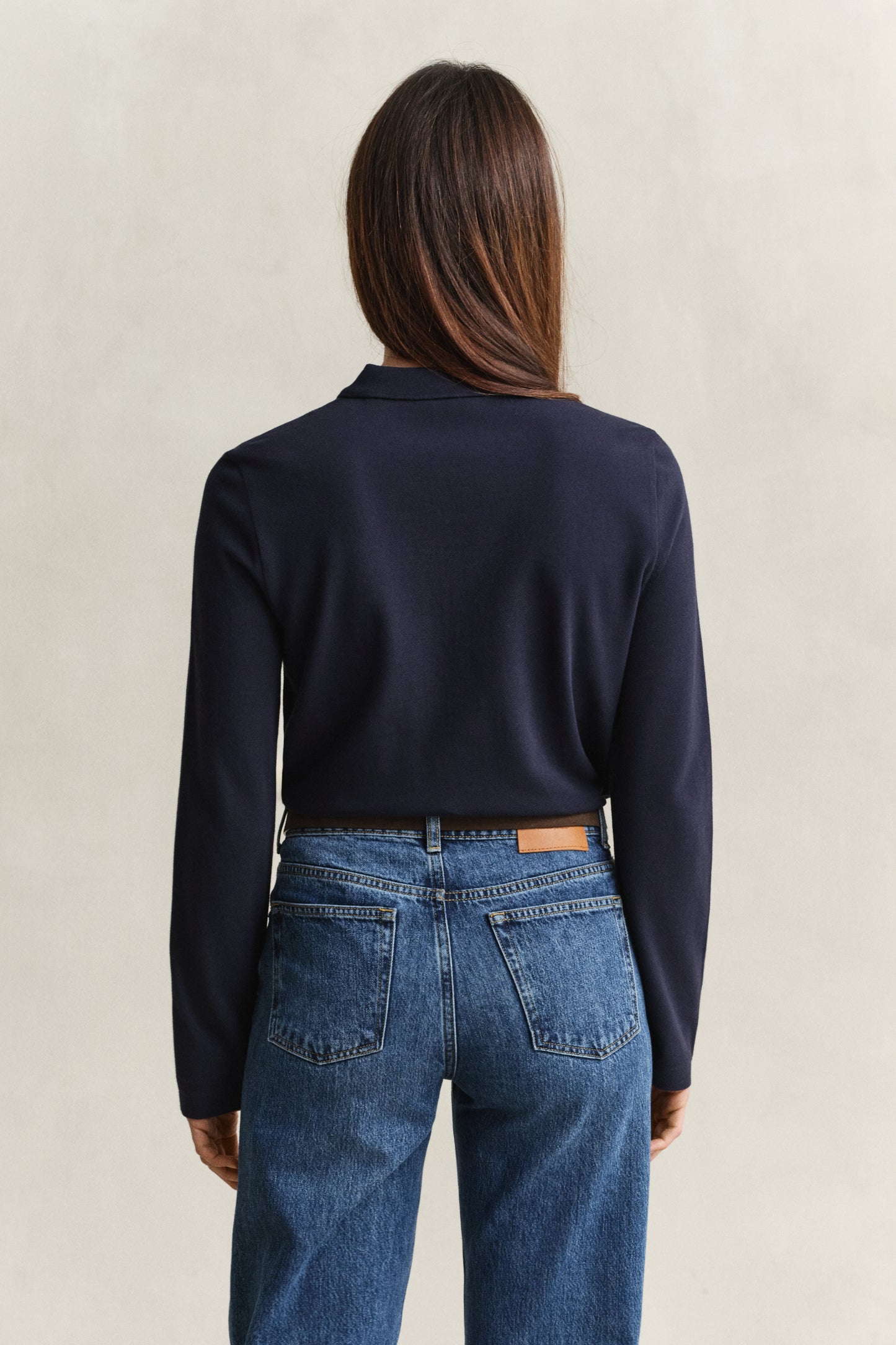 Person wearing a navy sweater and blue jeans on a beige background