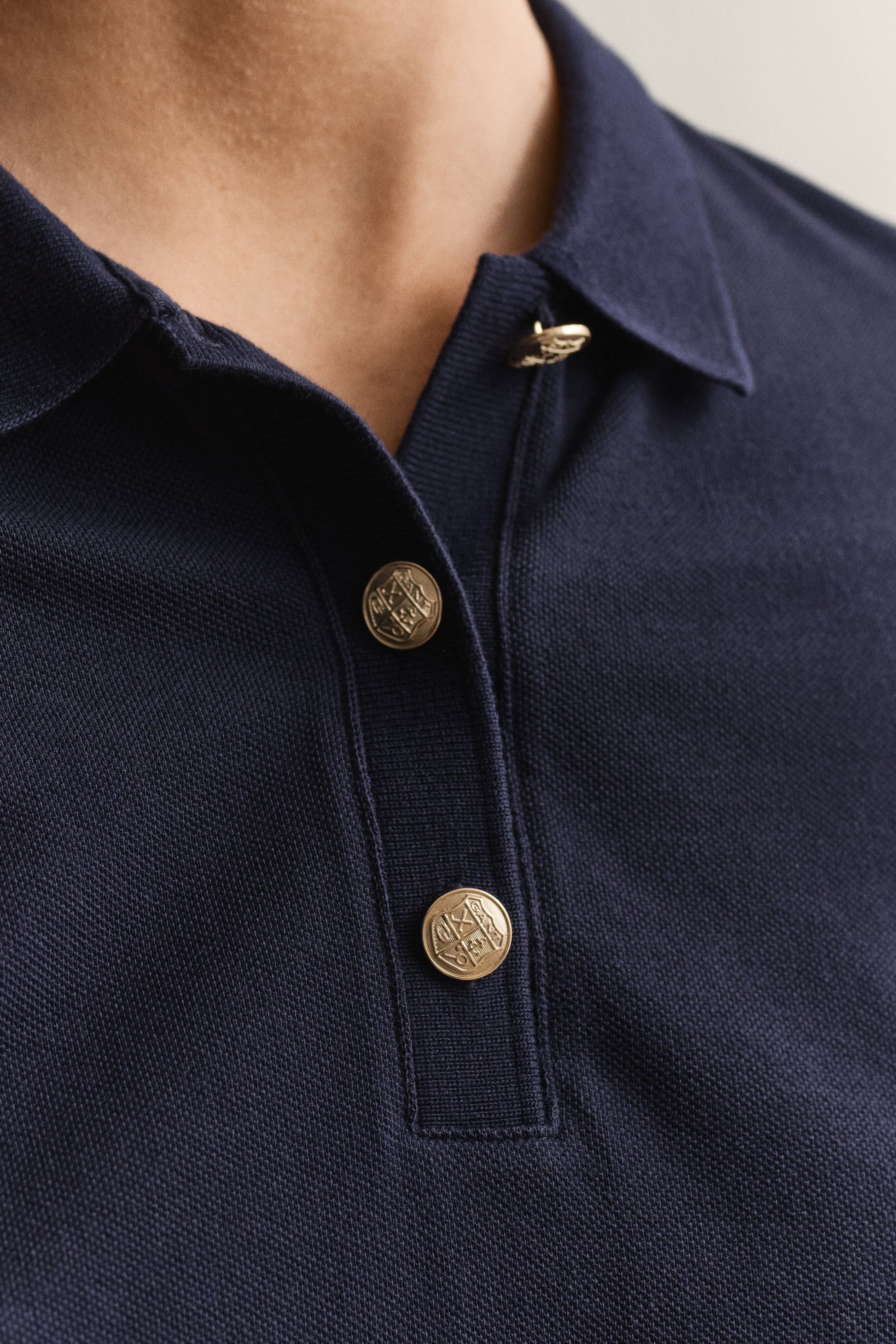 Navy blue polo shirt with gold buttons on a neutral background