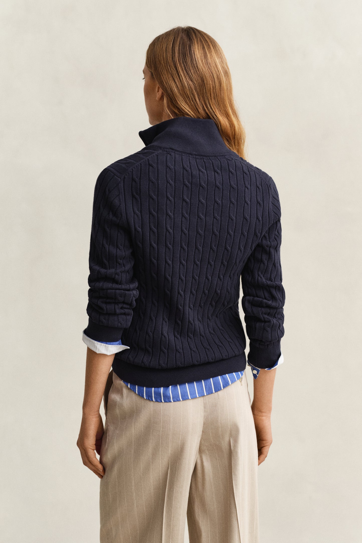 Person wearing a navy cable knit sweater over a blue shirt with beige pants on a light background