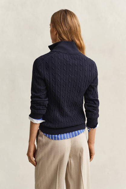 Person wearing a navy cable knit sweater over a blue shirt with beige pants on a light background