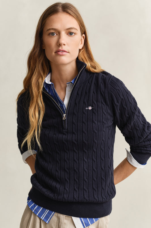 Woman wearing a navy cable knit sweater with a beige background