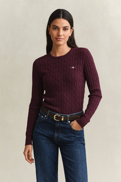 Woman wearing a maroon sweater with a logo and blue jeans on a beige background