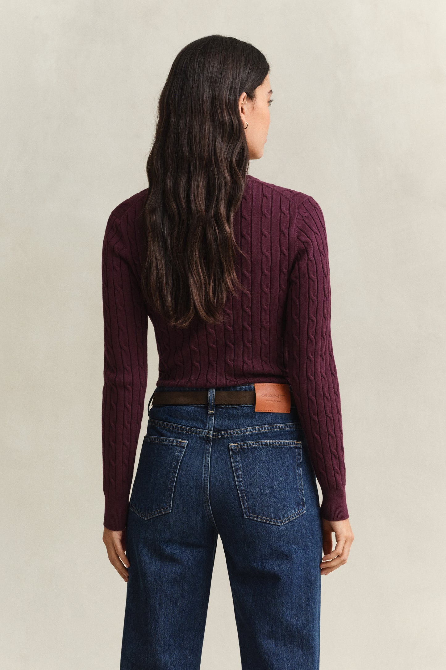 Woman wearing a burgundy cable knit sweater and blue jeans on a beige background