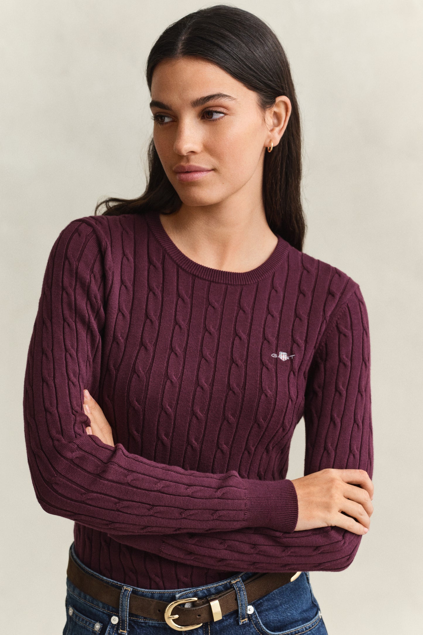 Woman wearing a maroon cable knit sweater with a visible brand logo on a neutral background