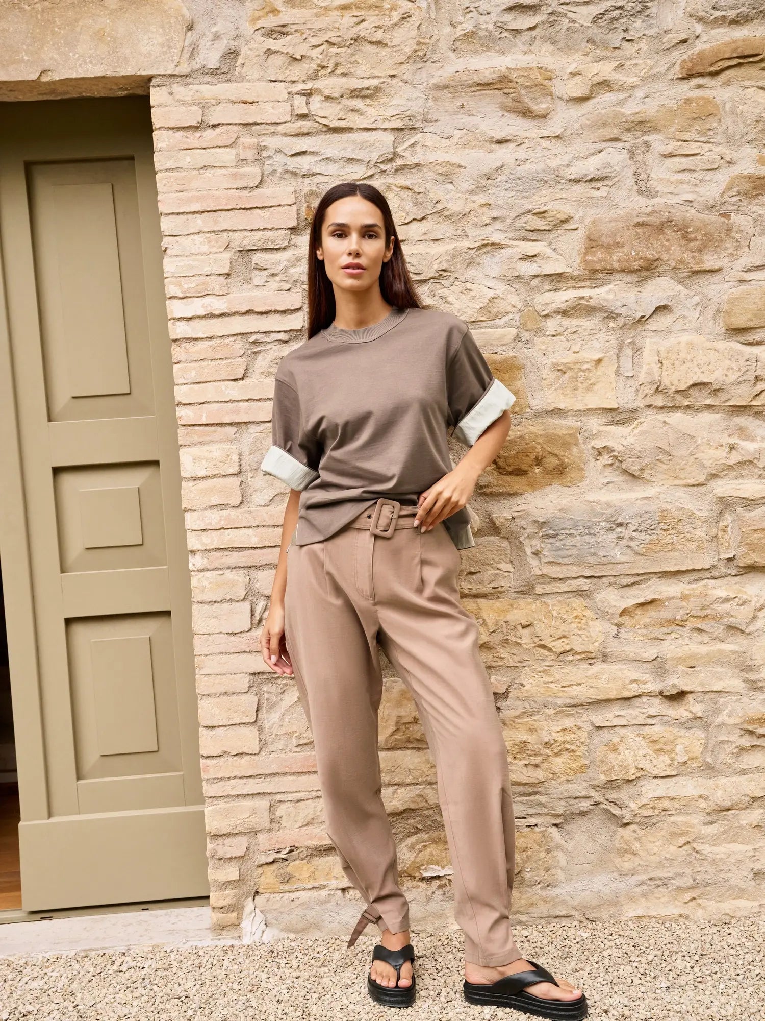 Woman in a brown outfit standing against a stone wall.
