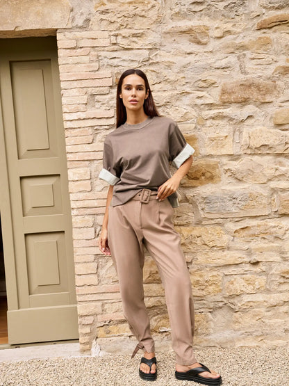 Woman in a brown outfit standing against a stone wall.
