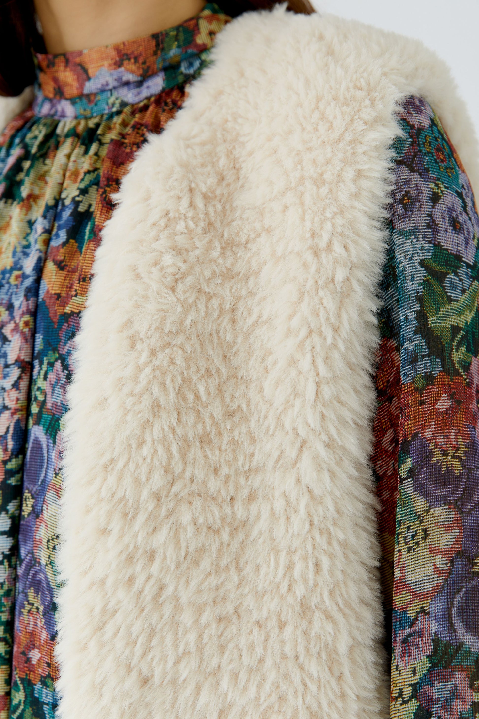 Close-up of a cream faux-fur vest layered over a colorful floral printed dress.