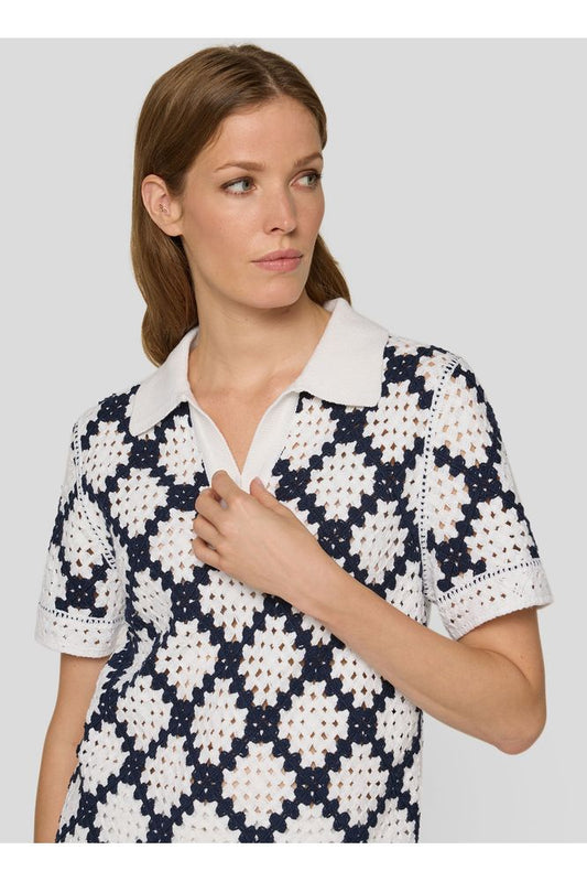 Woman wearing a navy and white patterned crochet top against a plain background