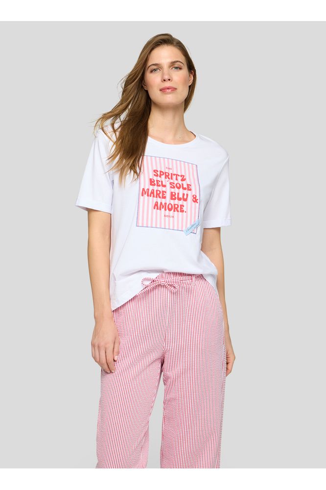 Woman wearing a white t-shirt with red text and pink checkered pants on a gray background
