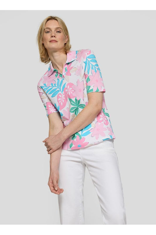 Woman wearing a colorful floral blouse and white pants on a plain background