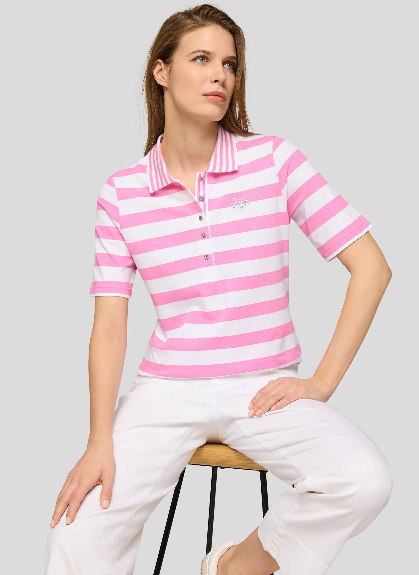 Woman wearing a pink and white striped polo shirt and white pants on a gray background