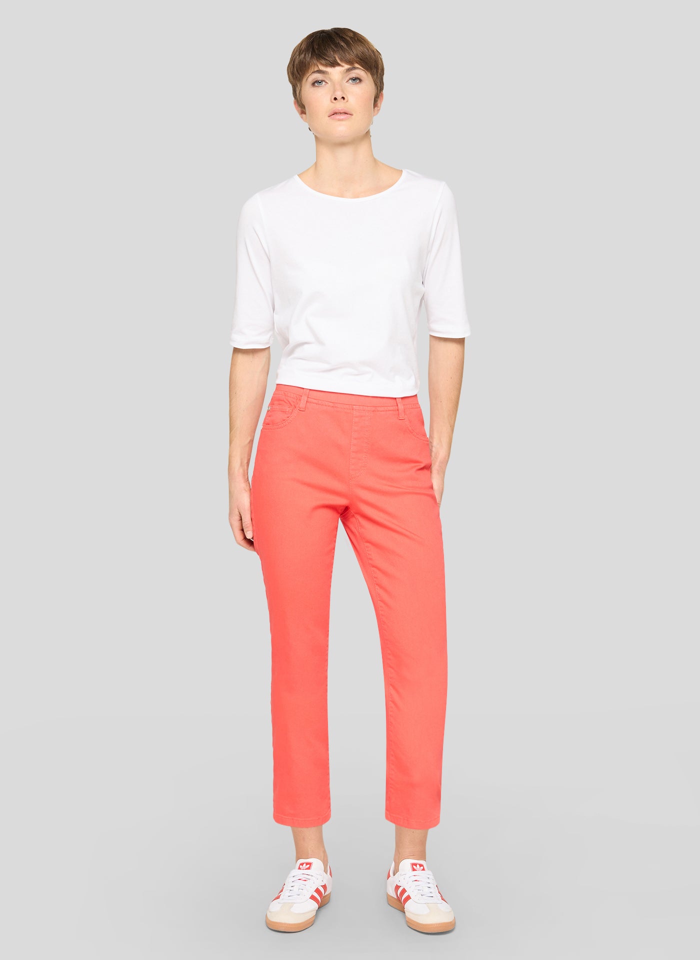 Person wearing a white top and coral pants on a gray background